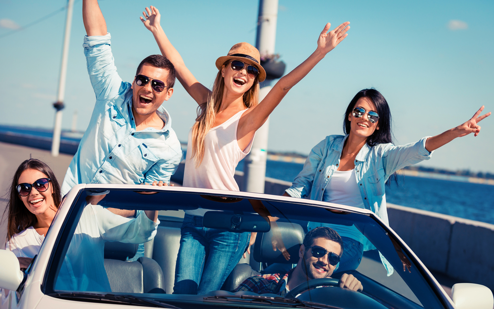 Friends in convertible. Group of young happy people enjoying road trip in their white convertible and raising their arms