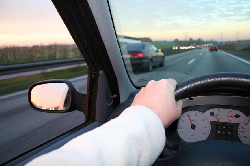driving steering car. hand holding wheel whilst car overtaking. drive at dusk with sunset in horizon