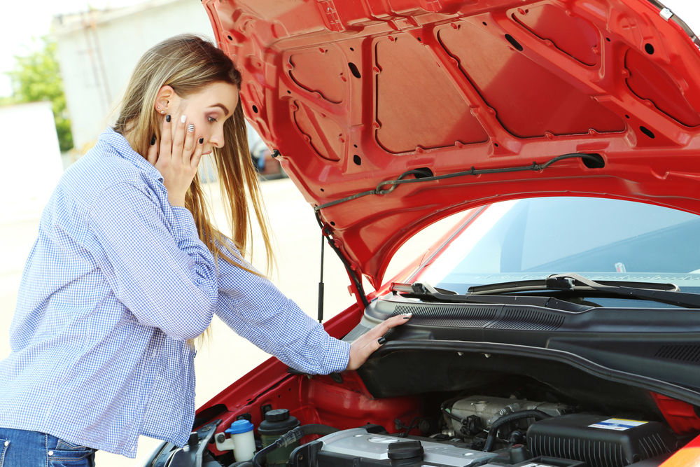 Beautiful young girl open hood of broken car